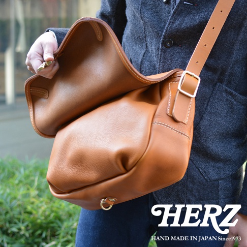 皮革復古翻蓋郵差包，棕褐色，附可調式肩帶和金屬扣環，手工縫線，展現皮革自然紋理。