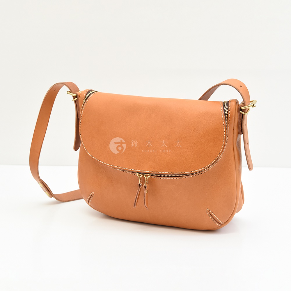 一個棕褐色的皮革側背包，上面有兩個拉鍊，以及品牌標誌「鈴木太太」和「SUZUKI SHOP」。