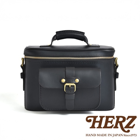 HERZ 職人手作黑色皮革相機包，正面有一個帶有金色釦環的翻蓋口袋，頂部有皮革提把。
