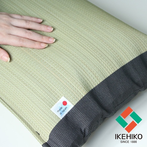 淺綠色藺草編織的枕頭，帶有深灰色條紋滾邊，左上方有一張標示「made in Japan」的小標籤，右下方有 IKEHIKO 品牌標誌。