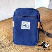 石洗帆布斜背手機包，藍色，配有皮革飾邊和可調節斜背帶，包身中央有方形布貼，印有日文圖案和文字。