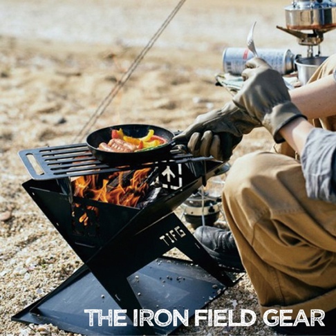 TAKI BEITA焚火台爐架套裝S，黑色金屬材質，設計成可折疊的X型結構，上方放置有烤網，烤網上有一鍋正在烹煮香腸和甜椒的鑄鐵鍋。