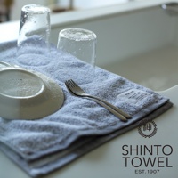 YUKINE 雪中漫步有機棉蓬厚浴巾，淺灰色，質地蓬鬆柔軟，上面擺放著兩個沾有水珠的玻璃杯、一個白色盤子和一把銀色叉子。