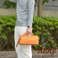 職人手作皮革長型迷你醫生包 CW-106，採用天然皮革製成，呈現溫潤的淺棕色。包款設計簡潔，配有頂部提把、可調節肩帶及金屬鎖扣，側面可見釘狀裝飾，整體散發經典復古氣息。