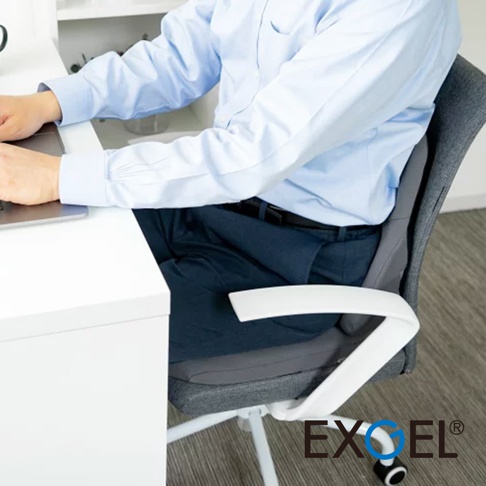 THE OWL 貓頭鷹基本款背墊，灰色布面，搭配白色椅背扶手，展示於辦公椅上，一位穿著淺藍色襯衫與深藍色褲子的男士正坐在上面使用筆記型電腦。