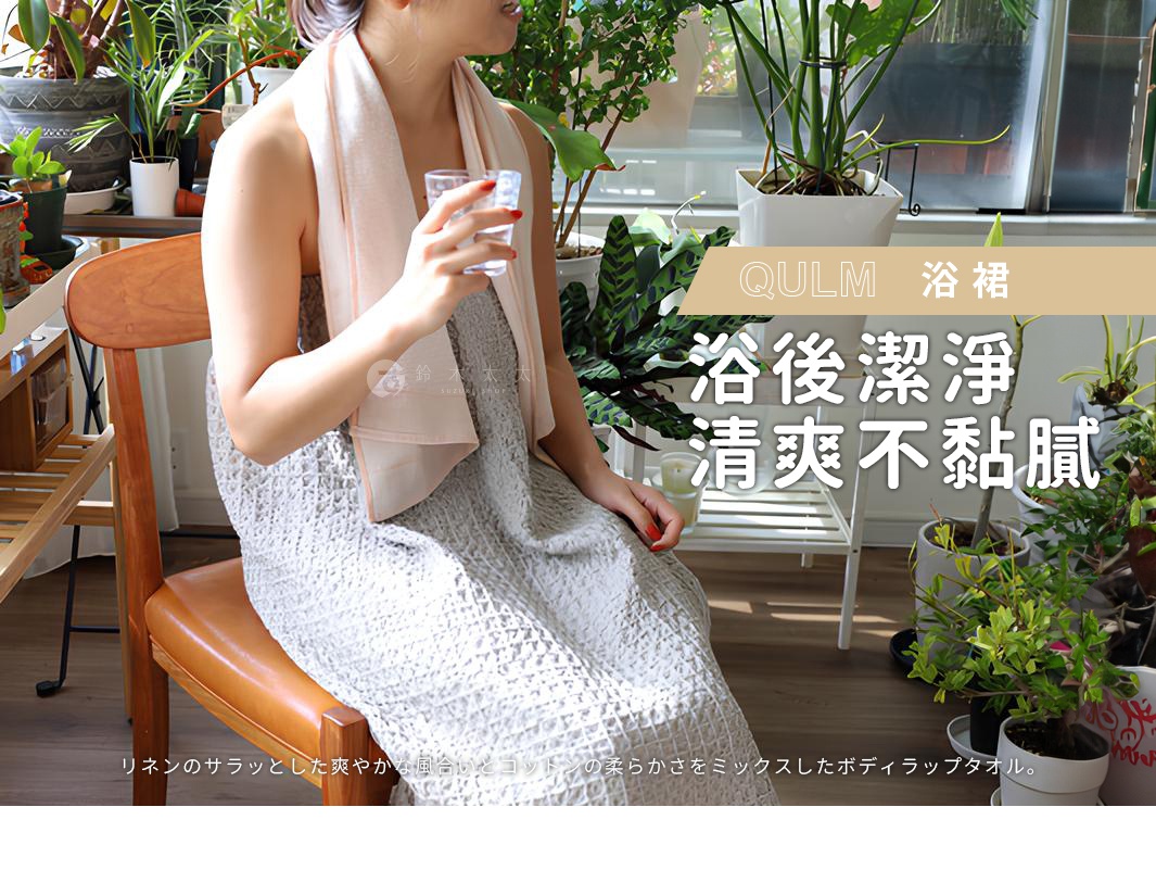 一位女子身著平口浴裙，肩披淺粉色浴巾，手持一杯水，坐在木椅上。浴裙為淺灰色網狀織紋，浴巾為素面，質感柔軟。背景為綠植環繞的室內空間。