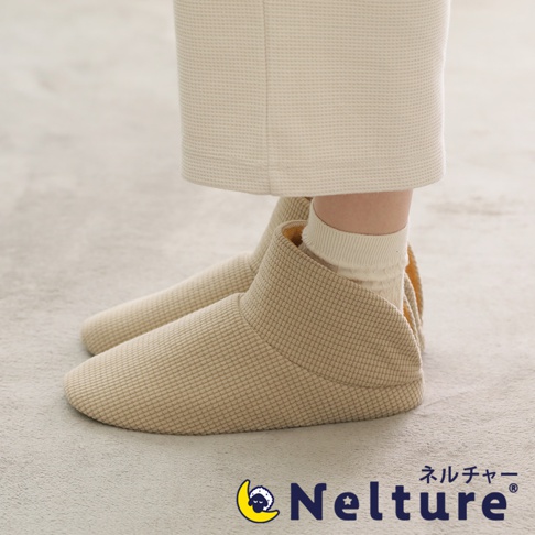 一雙米色網格紋路的保暖腳踝室內拖鞋，鞋面材質柔軟，鞋口設計包覆腳踝，搭配同色系襪子，整體呈現溫馨舒適的居家風格。
