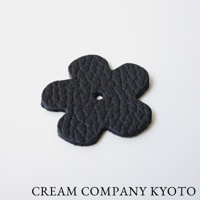 京都職人手作的黑色皮革花朵造型吊飾，表面有細緻紋理，中心有一個圓形孔洞，可用於收納包的裝飾或配件。