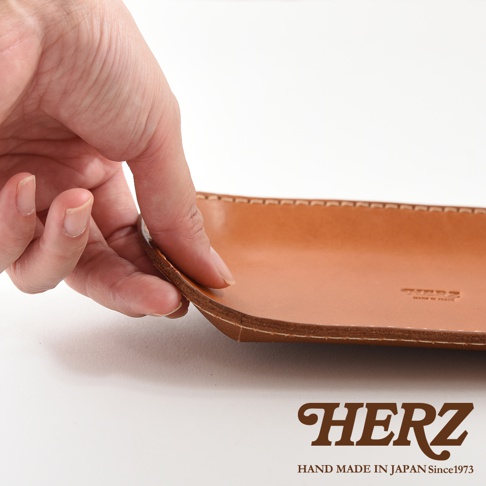 職人手作皮革小物收納盤，淺棕色皮革，邊緣縫線整齊，表面光滑，品牌標誌烙印其上。