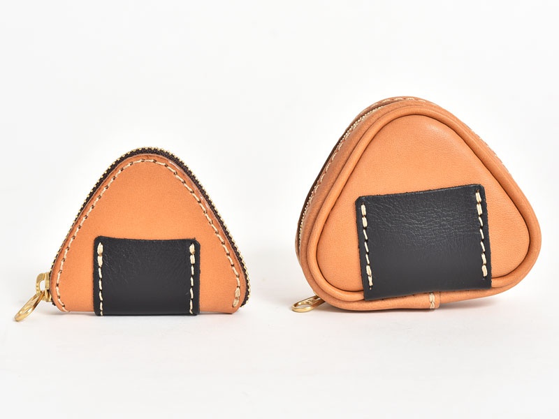 兩個淺棕色牛皮製作的三角飯糰造型零錢包，一前一後並列。表面皆有黑色皮革小方塊裝飾，以白色車線縫合。零錢包皆有金色拉鍊。