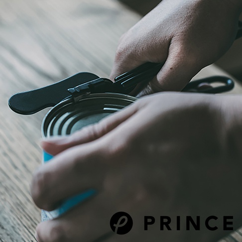 一隻手正握著黑色金屬旋轉開罐器，使用它來開啟罐頭頂部的蓋子。