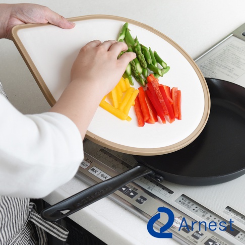 淚滴型抗菌料理砧板，白色表面，帶有淺褐色邊框，上面擺放著切好的蘆筍、黃甜椒和紅甜椒。