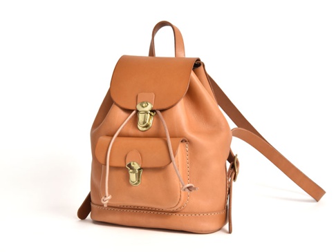 職人手作皮革經典迷你後背包，天然原色皮革，設有翻蓋主袋、束繩開口及前方小口袋，搭配金色旋轉鎖扣及可調式皮革背帶，風格復古簡約。
