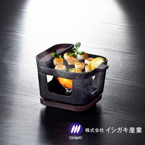 黑色鑄鐵烤盤鍋爐組，烤盤上擺放著多塊煎烤過的扇貝，旁邊配有檸檬片和綠葉裝飾。鍋爐下方有燃燒的火焰，整體置於深色木紋桌面上。