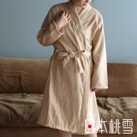 身著淺卡其色異素材紗質浴袍的女性，浴袍腰間繫有同色系腰帶，背景為沙發與藍色牆面。