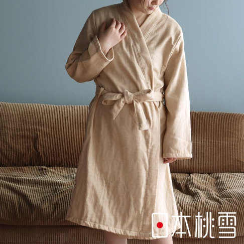 身著淺卡其色異素材紗質浴袍的女性，浴袍腰間繫有同色系腰帶，背景為沙發與藍色牆面。