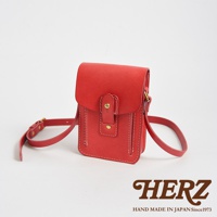 紅色皮革製成的職人手作休閒散步包，帶有可調節長度的皮革背帶，包蓋處有雙重按扣設計，包身側面有縫線裝飾。