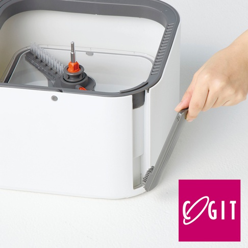 一隻手正將一個灰色的刷子配件安裝到白色方型拖把清潔桶的側邊，桶內可見橘色的旋轉軸心結構，右下角印有 COGIT 品牌標誌。