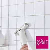 白色推拉瀝水刮刀，帶有灰色橡膠刮片，手柄上有圓形透氣孔，正被一隻手握住，用於清潔佈滿水珠的白色瓷磚牆面。