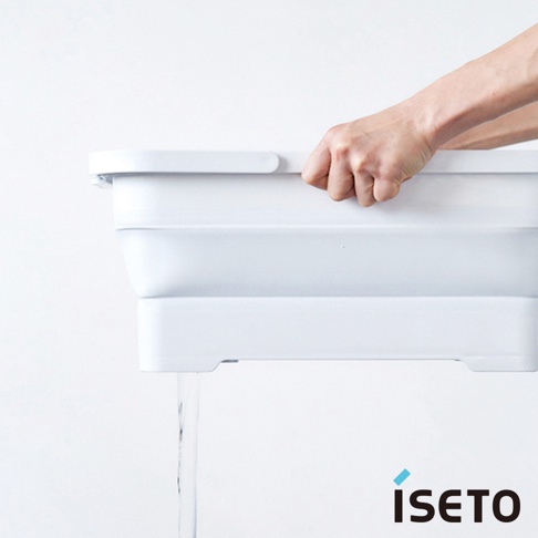 白色伸縮提籃，由塑膠製成，具有可折疊的結構，手持提籃邊緣，底部有水流出。