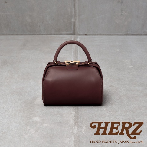 深棕色皮革手提包，帶有金色口金和提把，整體呈現醫藥包造型，質感紮實。