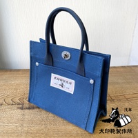 藍色純棉帆布迷你托特包，設有兩個提把、正面有兩個外袋，其中一個外袋上貼有印有日文文字和圖案的標籤，包包開口處有金屬旋轉鎖扣。