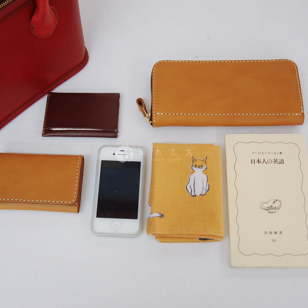 紅色皮革手提包、咖啡色短夾、棕色長夾、白色手機、黃色貓咪圖案布料，以及一本日文書。