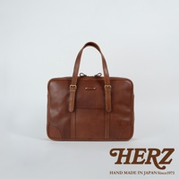 職人手作皮革肩背手提兩用公事包，採用經典棕色牛皮，款式簡約，配有雙提把、可調節肩帶扣環及品牌壓印標誌。