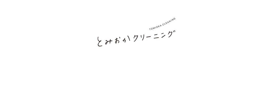 白色背景上，黑色手寫字體「とみおかクリーニング」及英文「TOMIOKA CLEANING」。