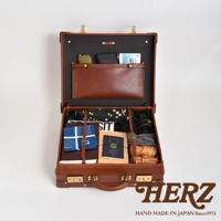 職人手作皮革英倫風便攜手提行李箱，開啟狀態，內部裝有護照、錢包、摺疊傘、相機及衣物等。行李箱為棕色皮革材質，搭配金色鎖扣與提把，內襯為黑色。