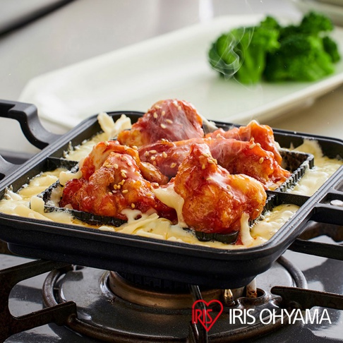 直火專用熱壓三明治夾烤盤，呈現黑色方形烤盤，內含烤製中的韓式炸雞塊，淋上融化起司，撒有白芝麻，周圍有蒸氣冒出，背景為白色盤子與一小撮綠色花椰菜。