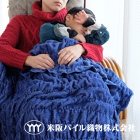 一件深藍色、波浪紋理的細絨毯子，覆蓋在一位身穿紅色毛衣的女性和一位熟睡的孩子身上。