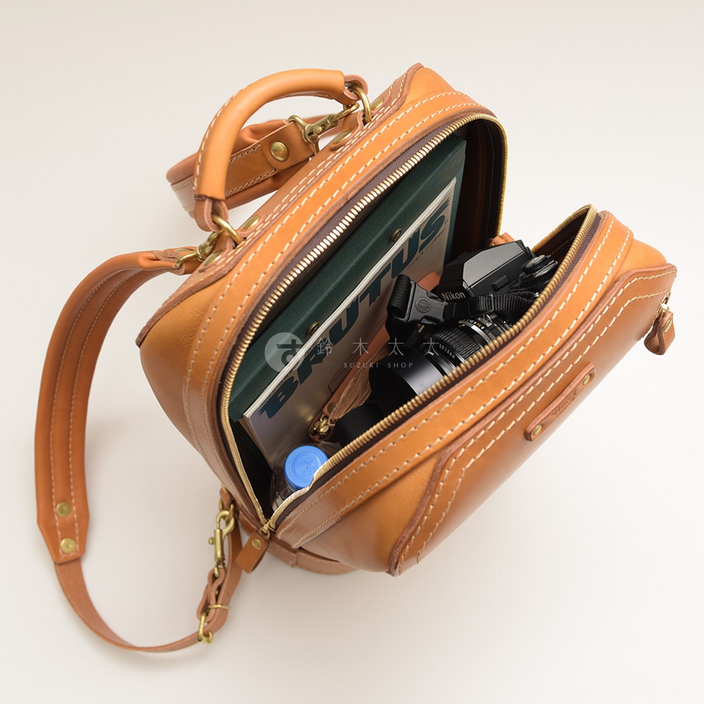 棕色皮革製成的立體商務後背包，內部裝有雜誌、相機和水瓶，展現其收納空間。