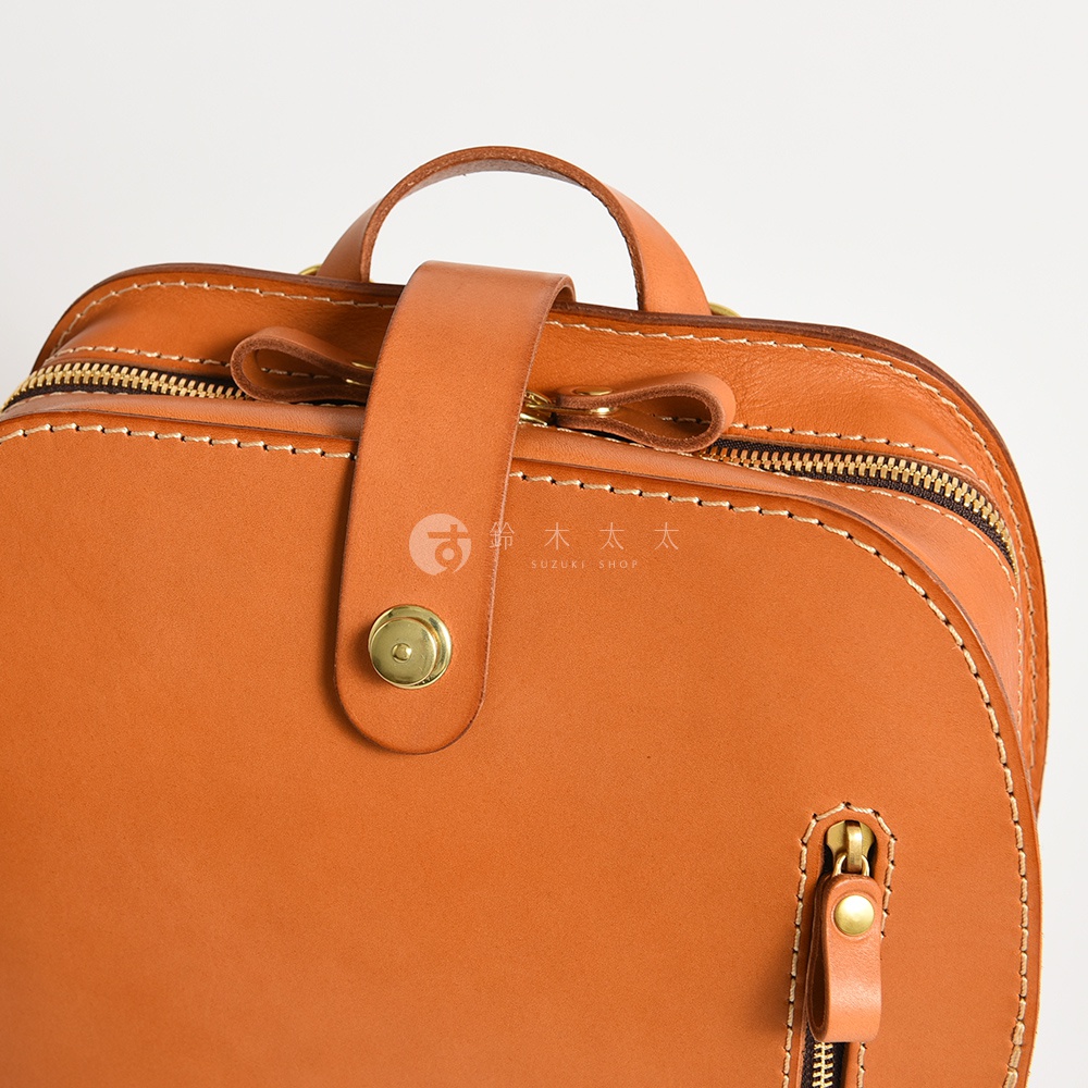 職人手作皮革商務休閒兩用後背包 R-36，採用溫暖的橘棕色皮革，搭配金色拉鍊和圓形金屬釦，展現精緻手感與復古質感。