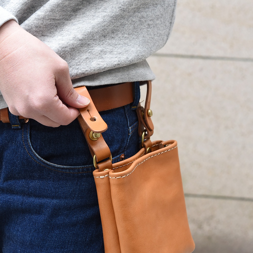 職人手作棕色皮革多用途工作用腰袋，以縫線裝飾，透過皮革腰帶固定於牛仔褲上。