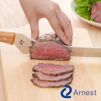 不鏽鋼麵包刀正被用於切片烤牛肉，刀身閃耀著金屬光澤，握柄為木質。盤中盛有切好的牛肉片和生菜。