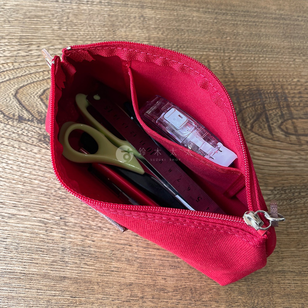 紅色石洗帆布小物收納包，內有綠色剪刀、尺、筆及白色修正帶，收納包為拉鍊式，內部有分隔層，材質為帆布。