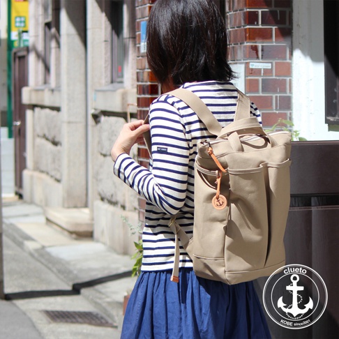 一名女子背著一個卡其色帆布後背包，背包上有皮革吊飾，側面有數個口袋。