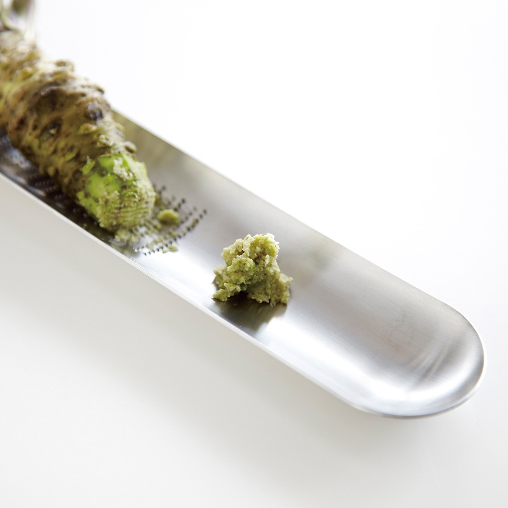 日製磨泥器，銀色金屬材質，上面放有一塊綠色山葵，下方有磨好的山葵泥。