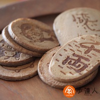 一堆圓形和橢圓形的鳥取手烤千兩煎餅，顏色呈淺棕色，表面烙有深棕色的圖案和漢字。