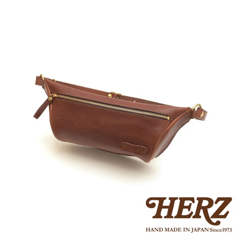 職人手作皮革輕便斜背包，採用鞣製牛皮製作，呈現溫潤的棕色皮革質感，搭配金色拉鍊與金屬扣環，設計簡約實用。