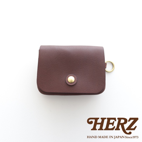 深棕色皮革雙層錢包，設有金色按鈕開合及側邊掛環，適合旅行使用。