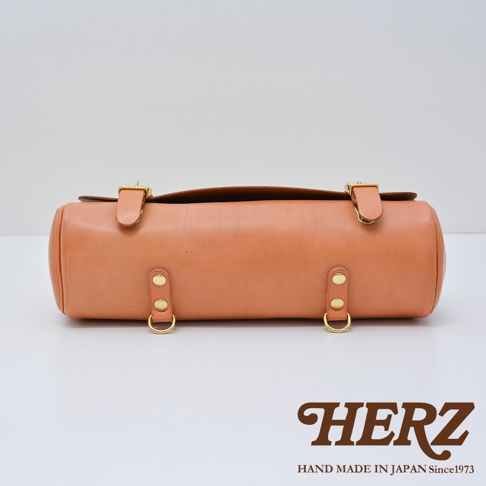 日本HERZ職人手作皮革屋瓦風側背包 CW-147，圓筒狀淺棕色皮革，兩側有金色扣環及D型環，上方有金色搭扣。