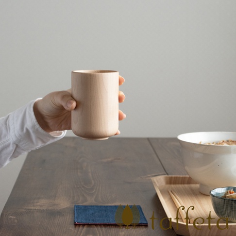 手持一個淺木色、圓柱形狀的楓木水杯，杯身光滑，頂部邊緣略微圓潤，呈現自然木紋。