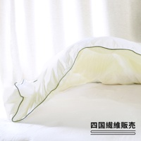 一張打開的雲絨被，被子為白色，邊緣有細緻的綠色滾邊，被子內部呈現淡黃色，整體鋪在白色的床單上，背景為白色窗簾。