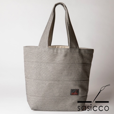 三河木綿刺子織大容量托特包，以黑白細格紋圖案為主，搭配水平縫線，設有寬版提把。包身角落有紅色品牌標籤。