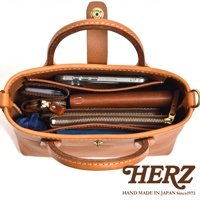 職人手作皮革迷你托特包 T-11，展示包內物品：手機、長夾、錢包、鑰匙包、藍色收納袋。包身為棕褐色皮革，縫線明顯，質感佳。