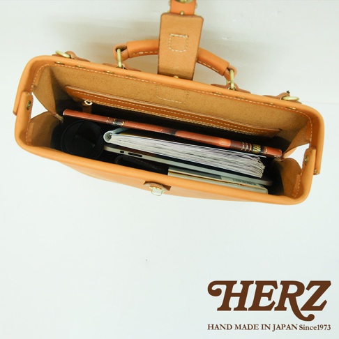 職人手作皮革軟式杜勒斯包，焦糖色皮革，包內裝有筆記本、筆、手機及其他小物。