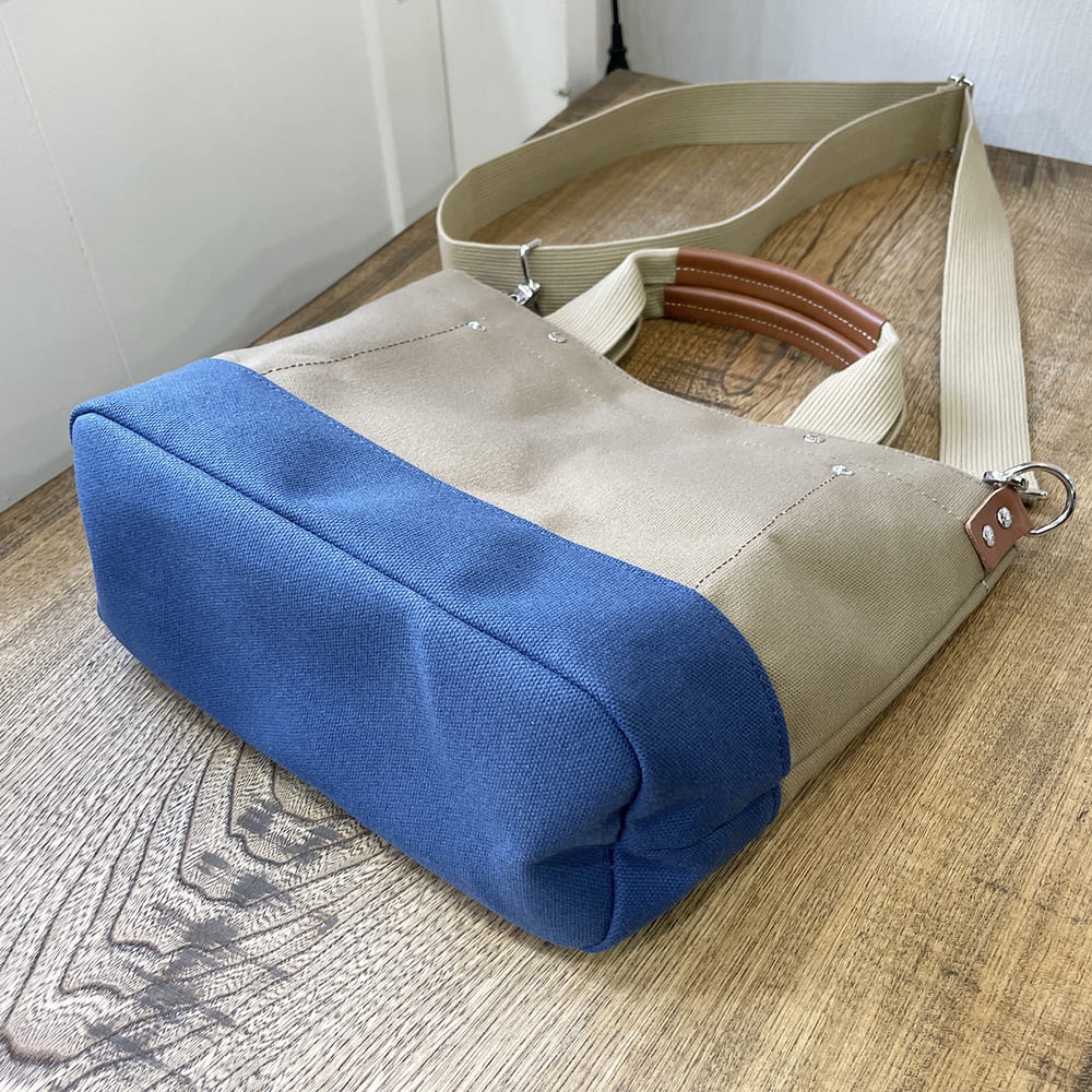 犬印純棉帆布兩用雙色托特包，主體為卡其色帆布，底部拼接藍色帆布，配有可拆卸的米白色帆布長背帶及棕色皮革手柄。