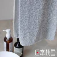 淺灰色毛巾，表面有細緻的環狀織紋，質地綿密。毛巾邊緣有細密的縫邊。背景有兩瓶沐浴用品，其中一瓶是帶壓頭的白色瓶裝，另一瓶是深色瓶裝。